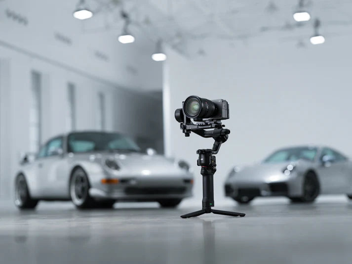 Camera on a tripod with two cars in the background in a showroom setting