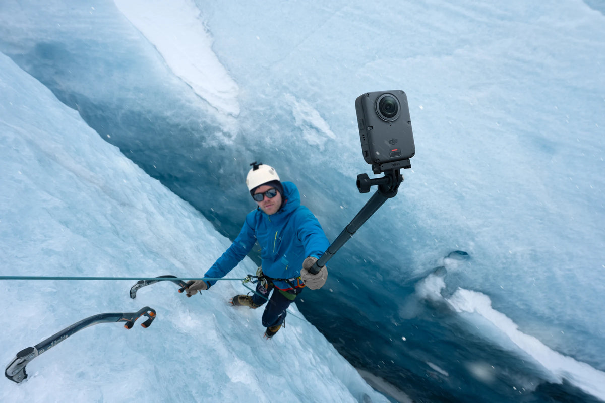 Ice climber holding a DJI Osmo 360 II on a pole beside a blue ice wall