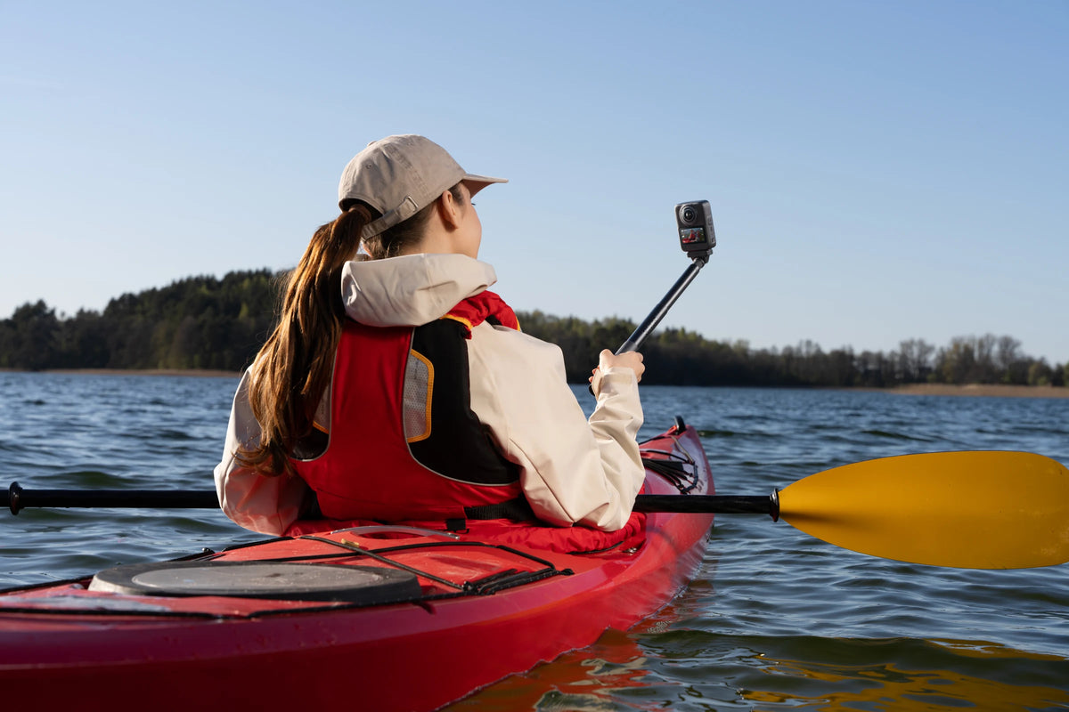 Kayaker holding a DJI Osmo 360 II on an extension pole while seated in a red kayak