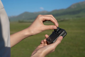 Hands replacing the outer lens on a DJI Osmo 360 II outdoors
